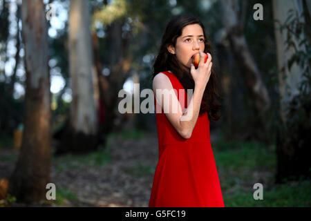 Giovane ragazza in abito rosso mangia un Apple all'aperto Foto Stock