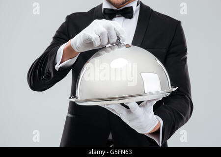 Primo piano del vassoio di portata con metallo cloche sostenuto da maggiordomi mani in guanti Foto Stock