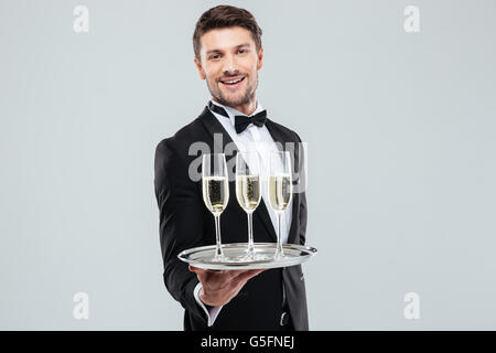 Allegro giovane maggiordomo in smoking sorridente e offrendo champagne Foto Stock