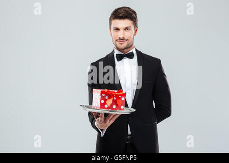 Bel giovane maggiordomo in smoking con papillon confezione regalo sul vassoio Foto Stock