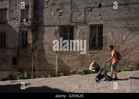 Padre spinge il bambino attraverso la mattina presto luce sulle pareti di architettura off Place de la Canourge nella vecchia Montpellier, Francia Foto Stock