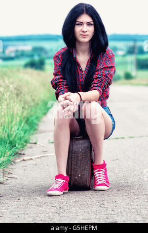 Ragazza in pantaloncini corti con una valigia sulla strada Foto Stock