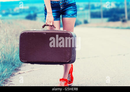 La ragazza con la valigia vintage è l'asfalto. Ragazza viaggiare autostop. Foto Stock