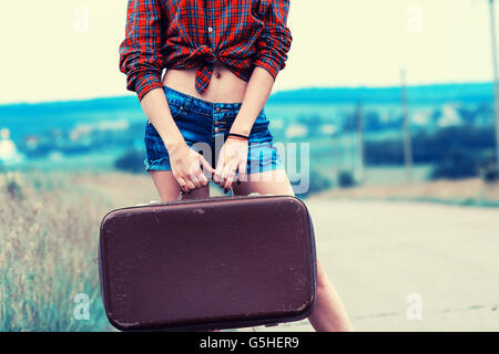 La ragazza con la valigia vintage è l'asfalto. Ragazza viaggiare autostop. Foto Stock