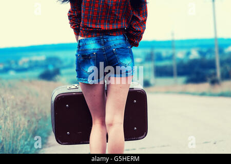 La ragazza con la valigia vintage è l'asfalto. Ragazza viaggiare autostop. Foto Stock