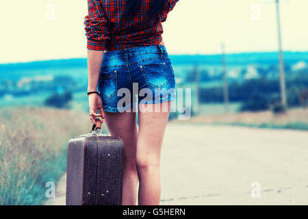 La ragazza con la valigia vintage è l'asfalto. Ragazza viaggiare autostop. Foto Stock