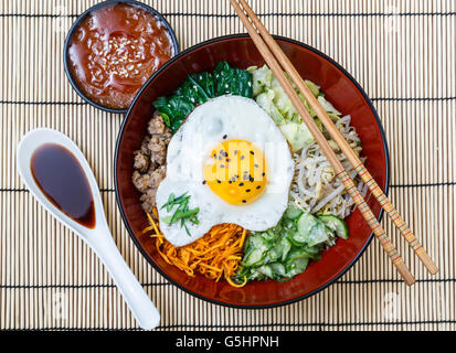 Bibimbap in una ciotola con salse sul tappetino di bambù, coreano piatto. Foto Stock