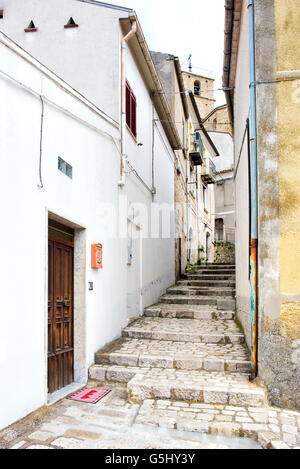 Vecchia stretta strada di ciottoli con gradini che conducono su per la collina tra gli edifici in un villaggio, vista dal fondo per la ricerca di Foto Stock