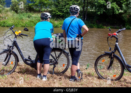 Due ciclisti anziani con le loro bici elettriche che guardano il fiume Foto Stock