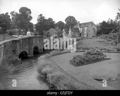 Una vista di un ponte che attraversa il fiume Colne a Bibury, Gloucestershire. Sullo sfondo è una vecchia casa mulino, con la strada che conduce a Cirencester. Foto Stock