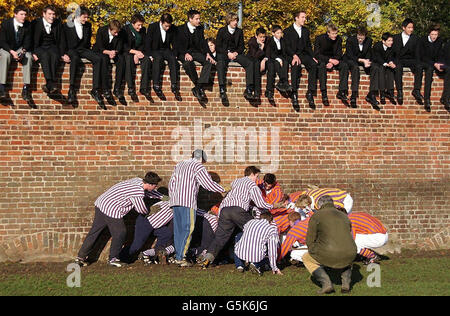 Gli alunni di Eton si siedono sul muro come umpire, il Dottor Michael Atkinson supervisiona bully mentre gli Oppidans disegnarono 0-0 con i Collegers nell'annuale St. Andrew's Day Eton Wall Game, all'Eton College, Berkshire. Il figlio del Principe di Galles, il Principe Harry, ha preso parte alla partita di quest'anno. Foto Stock