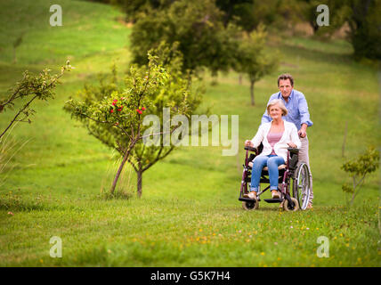 Senior uomo donna di spinta in carrozzella, verde la natura in autunno Foto Stock