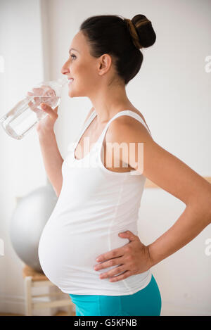 Incinta donna caucasici di bere acqua in bottiglia Foto Stock