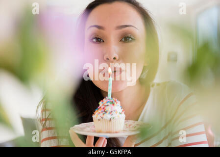 Donna di soffiaggio in fuori la candela di compleanno sul cupcake Foto Stock