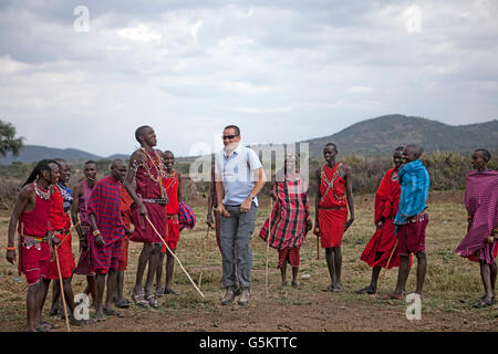 Un gruppo di guerrieri Masai e un turista facendo un cerimoniale di danza in un villaggio Maaai, Kenya, Africa. Foto Stock