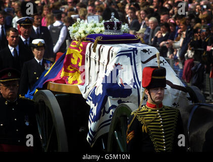 La bara della Regina Elisabetta la Regina Madre seguita dai membri della famiglia reale passando la statua di Re Giorgio VI sul Mall come viene portato da St James Palace a Westminster Hall dove giace in stato fino al funerale martedì prossimo. Foto Stock