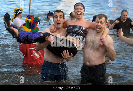 Una donna viene trasportata nell'acqua gelida da amici durante l'annuale immersione di Capodanno 'Loony Dook' nel Firth of Forth a South Queensferry, nr Edinburgh, Scozia. L'evento annuale si svolge a poche centinaia di metri dal famoso ponte ferroviario Forth. Foto Stock