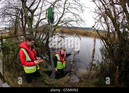 Gli idrologi Andrew Picken e Josh Johnstone (che tiene il personale dell'acqua indovinato) da Hydro Logic a Stirling, monitorano le attrezzature che forniscono informazioni per controllare i livelli dell'acqua sul fiume Forth ad Aberfoyle. Il Regno Unito è frenato per un altro giorno di deluges e inondazioni mentre pioggia e vento pesanti spazzano in tutto il paese. Foto Stock