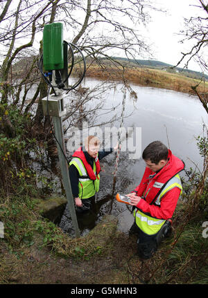 Gli idrologi Josh Johnstone (che tengono il personale dell'acqua guage) e Andrew Picken da Hydro Logic in Stirling, controllano l'apparecchiatura che fornisce le informazioni per sorvegliare i livelli dell'acqua sul fiume Forth ad Aberfoyle. . Il Regno Unito è accantanito per un altro giorno di deluges e di alluvioni mentre piogge e vento pesanti attraversano il paese. Foto Stock