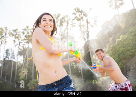 Coppia caucasica giocando con pistole per spruzzare sulla spiaggia Foto Stock