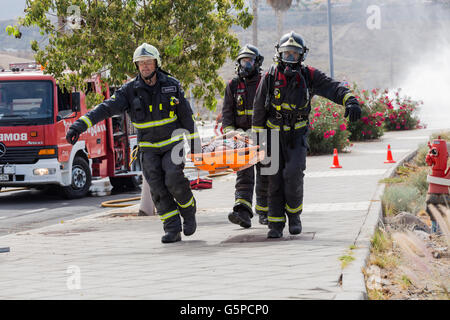 Il ramo di Adeje Tenerifes dei vigili del fuoco volontari di prendere parte ad una simulazione di emergenza di un incidente portano una vittima su una barella mentre pieno da indossare abbigliamento protettivo, Adeje, Tenerife, Isole Canarie, Spagna Foto Stock