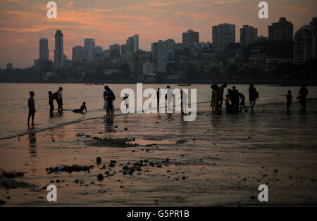 La gente del posto gioca in mare sulla spiaggia di Chowpatty mentre il sole tramonta dietro le colline di Malaba (il Manhatton di Mumbai) a Mumbai, India Foto Stock