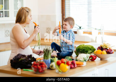 Donna incinta la preparazione di pasto con figlio da ortaggi freschi Foto Stock
