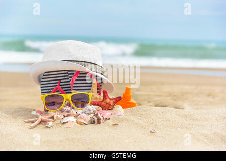 Occhiali da sole e un cappello su uno sfondo di conchiglie di mare. Foto Stock