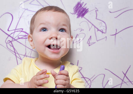 Smilling baby boy con pastelli a cera. Egli è alla ricerca per la fotocamera Foto Stock