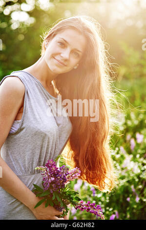 Sorridente ragazza tenendo un mazzo di fiori di lupino sul soleggiato Campo estivo Foto Stock