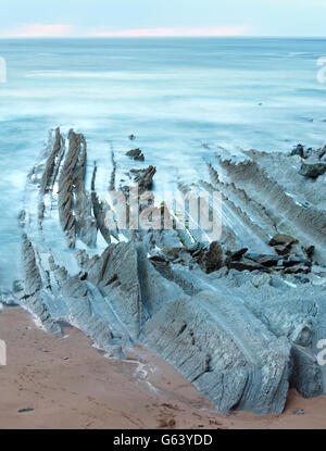 Twilight costa dell'oceano con stratiforme nervata formazioni rocciose. (Oceano Atlantico, Spagna). Foto Stock