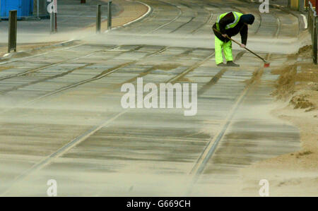 Un lavoratore soleggiato lotta per mantenere le piste del tram chiaro sul fronte mare di Blackpool, come alti venti coprono gran parte della passeggiata in sabbia. Foto Stock