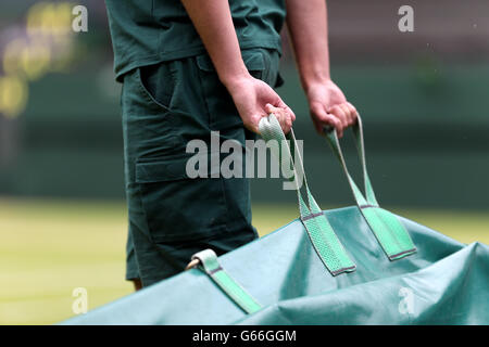 Groundstaff gara di mettere le coperture sul campo centrale come le fermate di pioggia giocare durante la partita tra Polonia Agnieszka Radwanska e la francese Mathilde Johansson durante il giorno quattro dei campionati di Wimbledon a tutta l'Inghilterra Lawn Tennis e Croquet Club, Wimbledon. Foto Stock