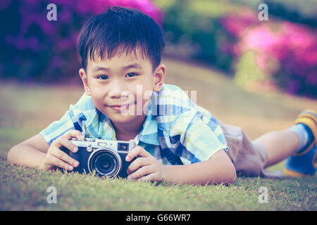 Bel ragazzo asiatico prendendo foto di vintage cinepresa, esplorare la natura al parco, in estate di giorno. Bambino in natura, ou Foto Stock