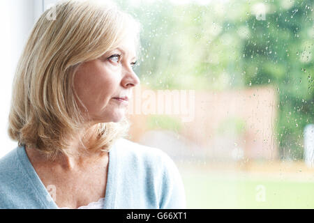 Triste donna matura che soffrono di agorafobia guardando fuori della finestra Foto Stock