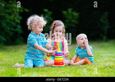 Tre piccoli giocare i bambini con colorati rainbow piramide giocattolo. Giocattoli educativi per i giovani bambini. I gemelli kids edificio torre Foto Stock