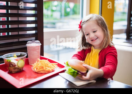 Bambina e ragazzo mangiare Chicken Nuggets, hamburger e patatine fritte in un ristorante fast food. Bambino con sandwich Foto Stock
