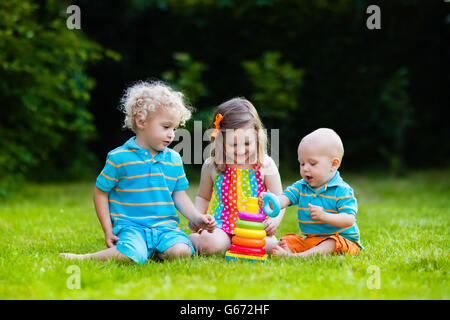 Tre piccoli giocare i bambini con colorati rainbow piramide giocattolo. Giocattoli educativi per i giovani bambini. I gemelli kids edificio torre Foto Stock