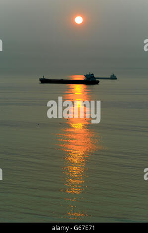 Il sole sorge su una nave al largo della costa nord-orientale vicino a Tynemouth, mentre i previsori dicono che il tempo sarà molto più caldo del solito per il periodo dell'anno. Foto Stock