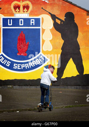 Un giovane ragazzo gioca su uno scooter accanto a un murales UDA Belfast dopo che l'Ulster Defense Association e l'Ulster Freedom Fighters hanno annunciato un cessate il fuoco di 12 mesi. Foto Stock