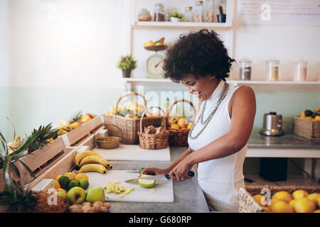 Colpo di giovane donna africana lavora al bar dei succhi e frutta di taglio. Barista rendendo succo di frutta fresco. Foto Stock