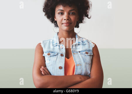Ritratto di giovane e bella donna in piedi con le braccia incrociate contro una parete. Fiducioso giovane africano modello femminile in smart c Foto Stock