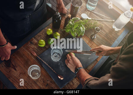 Primo piano delle mani baristi tagliare i limoni per preparare un cocktail. Due baristi sperimentando nuove ricette per cocktail a th Foto Stock