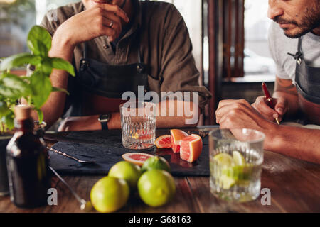 Immagine ravvicinata di due baristi seduti ad un tavolo con gli ingredienti per la realizzazione di cocktail. I baristi a sperimentare con la creazione di nuovi Foto Stock
