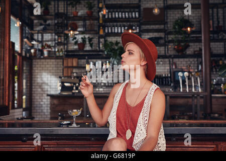 Ritratto di attraente giovane donna di fumare in un bar. Azienda di sigarette e di guardare lontano.