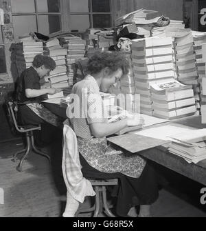 Degli anni Cinquanta, storico, due dei lavoratori di sesso femminile seduto al grippaggio panche giù di una pagina su sezioni di libri. Foto Stock