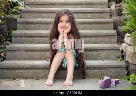 Piccola ragazza con i capelli lunghi seduto sui gradini Foto Stock