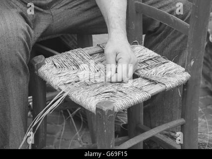 Le mani di un mender di sedie durante la riparazione di una vecchia sedia con paglia Foto Stock