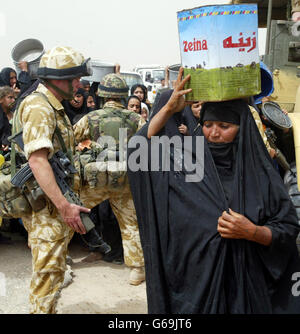 Una donna porta via l'acqua mentre altre attendono in coda con dei contenitori vuoti che sperano di riempire da una petroliera, mentre i soldati del Pioneer Regiment britannico del 23 sorvegliano la linea nella città irachena meridionale di Safwan. * le forze britanniche stanno aiutando la popolazione locale con aiuti umanitari. Foto Stock