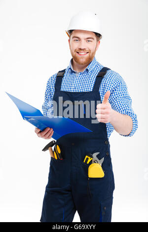 Sorridente giovane di successo builder utilizzando clipboad e mostrando pollice in alto Foto Stock